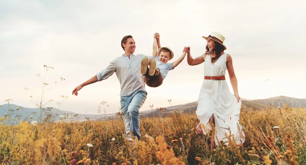 Smiling parents swinging their young son between them in a sunlit meadow