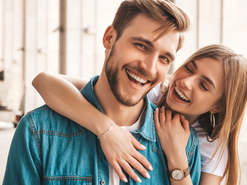 Laughing young woman hugging her boyfriend from behind